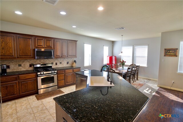 kitchen with stainless steel appliances, light hardwood / wood-style floors, sink, tasteful backsplash, and an island with sink