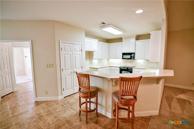 1802 N Vine St, Victoria, TX 77901 - kitchen with black microwave, range, a peninsula, white cabinetry, and light countertops