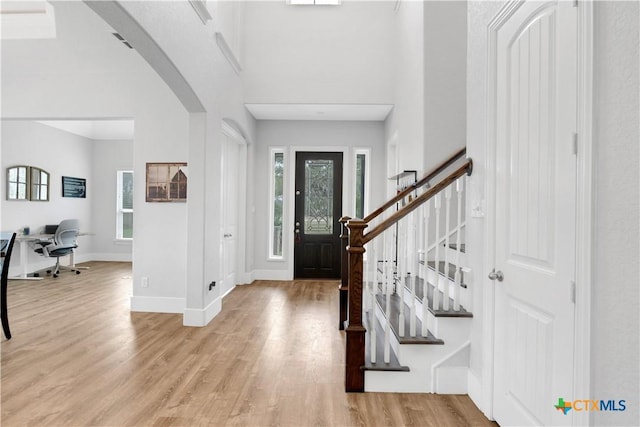 entryway featuring arched walkways, baseboards, stairs, and light wood-type flooring