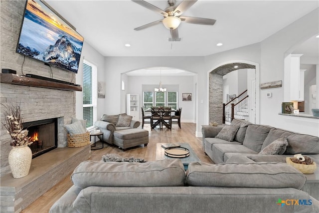 living area featuring stairs, arched walkways, wood finished floors, and ceiling fan with notable chandelier