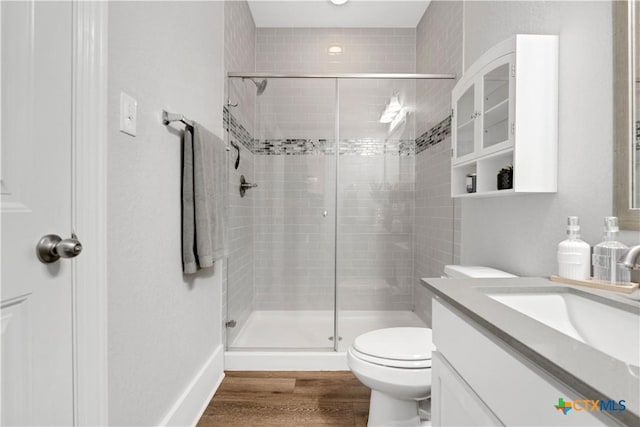 bathroom featuring wood finished floors, a shower stall, toilet, and vanity
