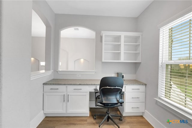 office space featuring baseboards, light wood-style flooring, arched walkways, and built in study area