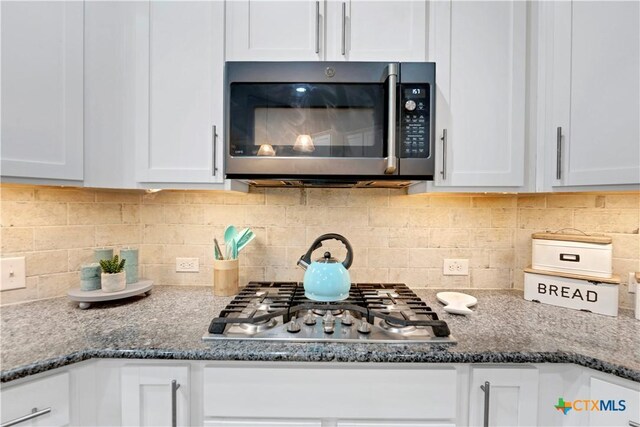 details featuring tasteful backsplash, white cabinets, stainless steel appliances, and dark stone counters