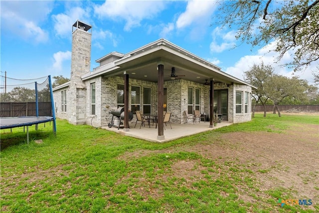 back of property with a trampoline, a fenced backyard, a yard, ceiling fan, and a patio