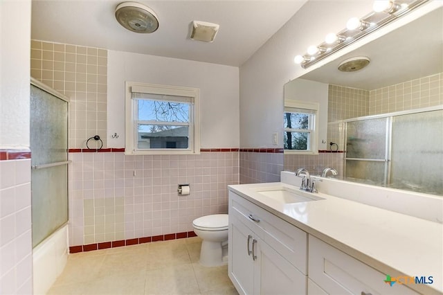 bathroom with toilet, tile walls, tile patterned flooring, enclosed tub / shower combo, and vanity