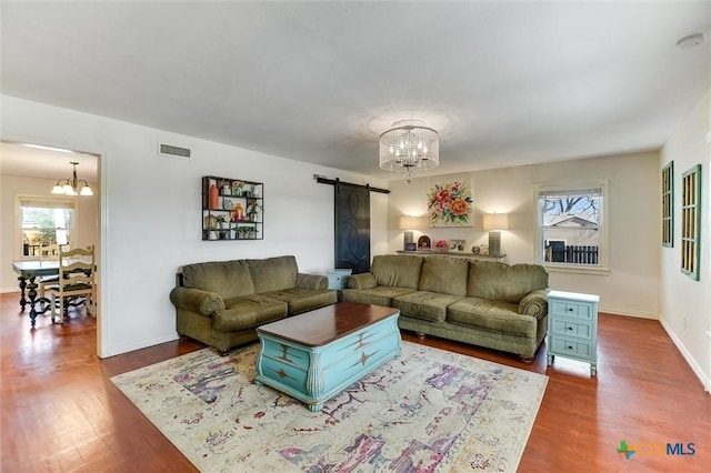 living room featuring visible vents, baseboards, a chandelier, a barn door, and wood finished floors