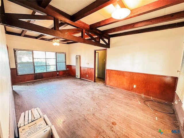 empty room with wood-type flooring, beamed ceiling, ceiling fan, and wooden walls