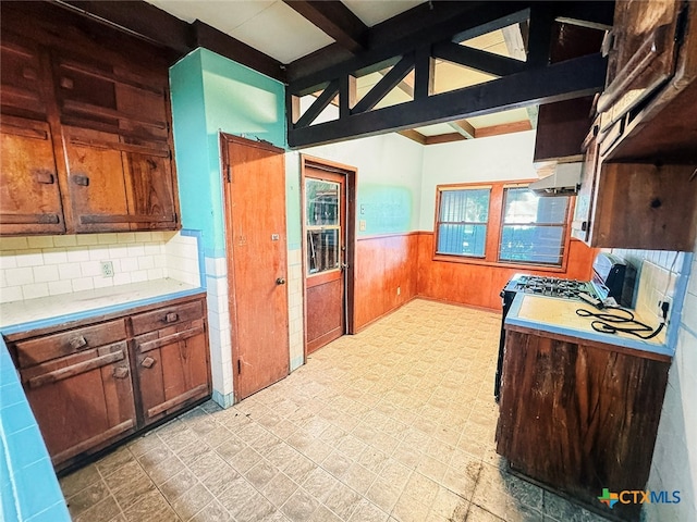 kitchen featuring exhaust hood, decorative backsplash, wood walls, and beam ceiling