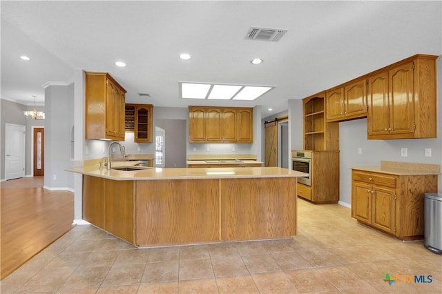 kitchen with a barn door, visible vents, oven, a peninsula, and a sink