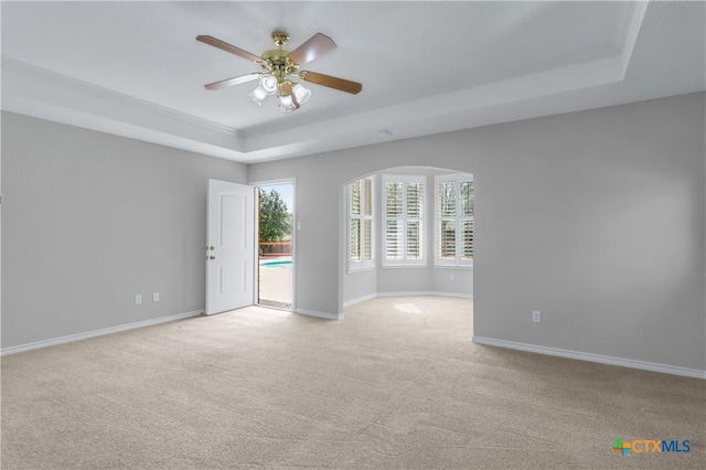 spare room with a tray ceiling, light colored carpet, arched walkways, and baseboards