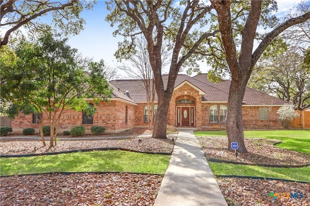 view of front of home featuring brick siding, fence, a front lawn, and roof with shingles