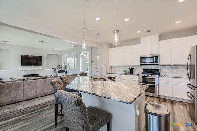 kitchen with light stone countertops, appliances with stainless steel finishes, sink, pendant lighting, and a center island with sink