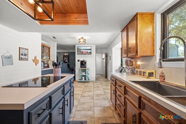 kitchen featuring brown cabinets, black electric stovetop, a raised ceiling, light countertops, and a sink