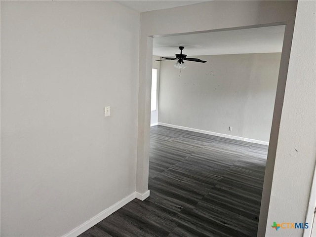 empty room with baseboards, a ceiling fan, and dark wood finished floors