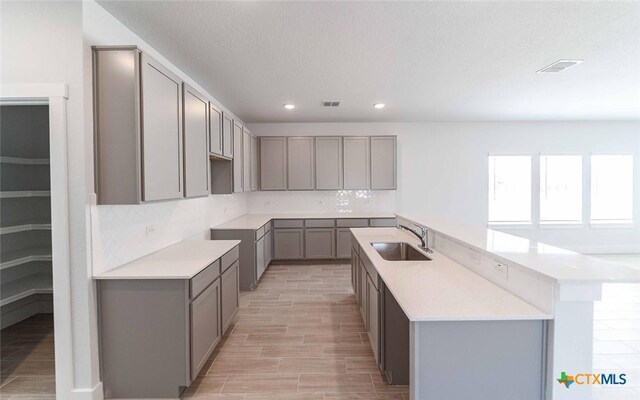 513 Lina Way, Seguin, TX 78155 - kitchen with a sink, gray cabinetry, a center island with sink, backsplash, and recessed lighting