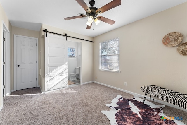 bedroom with ceiling fan, ensuite bathroom, a barn door, and carpet flooring