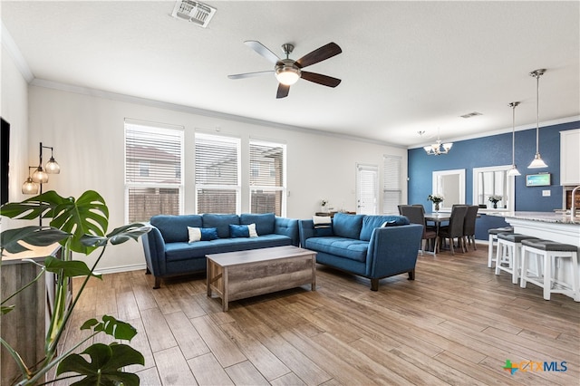 living room with visible vents, light wood-style floors, ornamental molding, and ceiling fan with notable chandelier