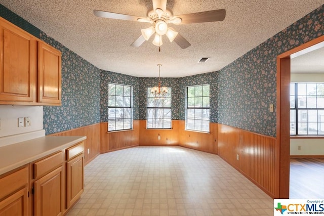 121 S Scenic Loop, Canyon Lake, TX 78133 - unfurnished dining area with a textured ceiling, plenty of natural light, light floors, a wainscoted wall, and a chandelier