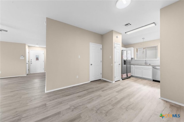 unfurnished living room featuring baseboards, visible vents, a sink, and light wood finished floors