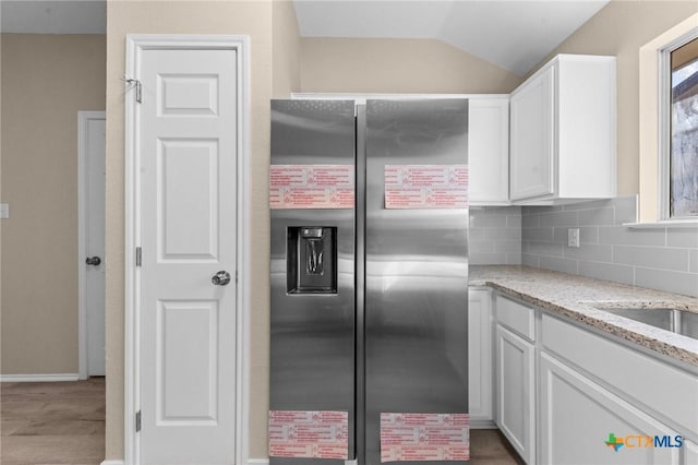 kitchen featuring light stone counters, stainless steel refrigerator with ice dispenser, decorative backsplash, white cabinets, and vaulted ceiling