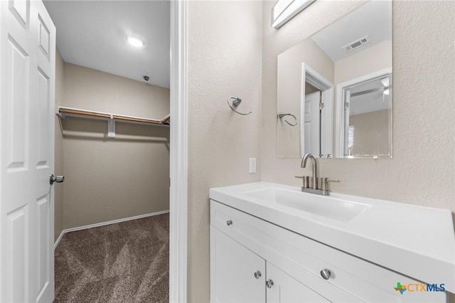 bathroom with baseboards, visible vents, a textured wall, a walk in closet, and vanity