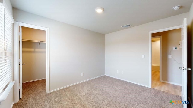 unfurnished bedroom with a walk in closet, light carpet, and a closet