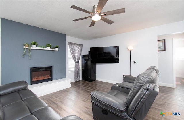 living area with a glass covered fireplace, baseboards, wood finished floors, and ceiling fan