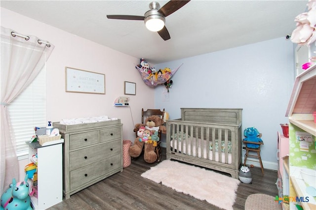 bedroom featuring baseboards, a crib, ceiling fan, and wood finished floors