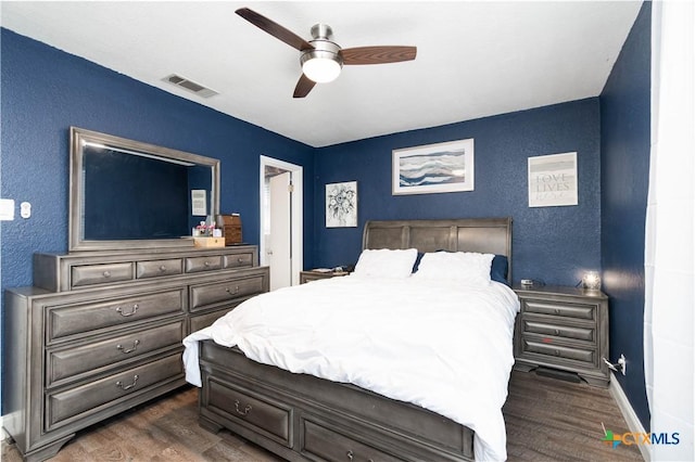 bedroom with ceiling fan, visible vents, dark wood finished floors, and a textured wall