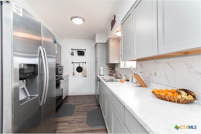 kitchen featuring dark wood-style flooring, a sink, light countertops, appliances with stainless steel finishes, and backsplash