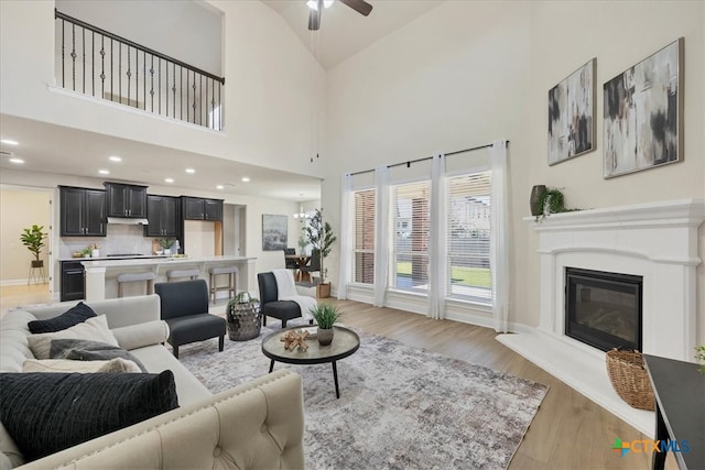 living room with ceiling fan, light wood-type flooring, and high vaulted ceiling