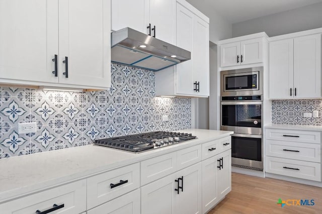 kitchen with light wood-type flooring, backsplash, stainless steel appliances, and white cabinetry