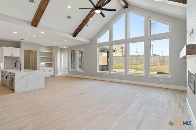 unfurnished living room with high vaulted ceiling, sink, light hardwood / wood-style flooring, ceiling fan, and beam ceiling