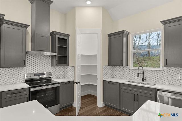 kitchen with appliances with stainless steel finishes, light countertops, gray cabinetry, wall chimney range hood, and a sink