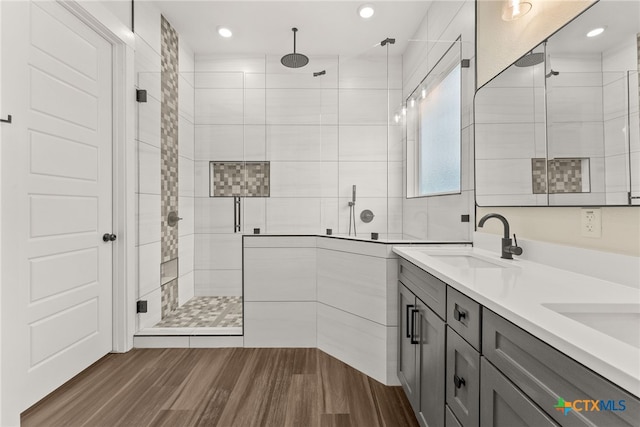 full bath featuring recessed lighting, wood finished floors, a sink, double vanity, and a stall shower