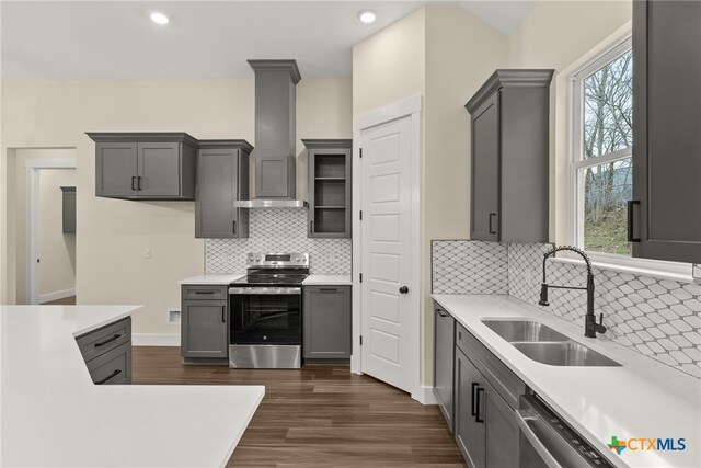 kitchen with light countertops, appliances with stainless steel finishes, wall chimney exhaust hood, and a sink