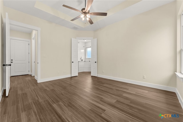 unfurnished bedroom with baseboards, a raised ceiling, and dark wood finished floors