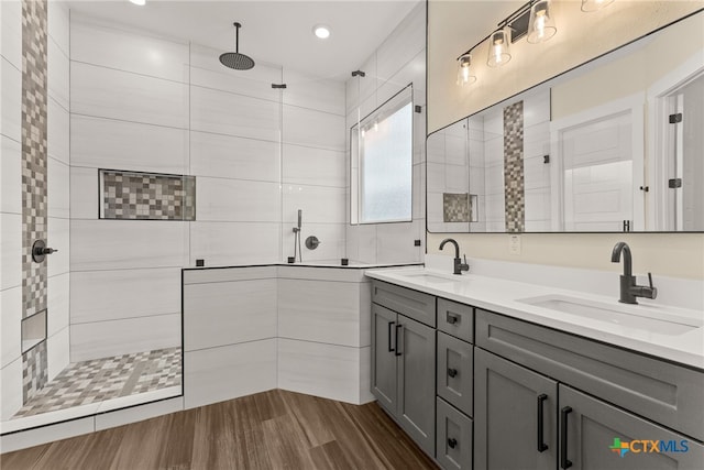 full bath featuring wood finished floors, double vanity, a sink, and walk in shower