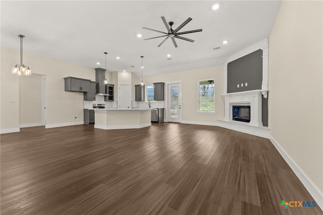 unfurnished living room with dark wood-style floors, recessed lighting, visible vents, a glass covered fireplace, and baseboards