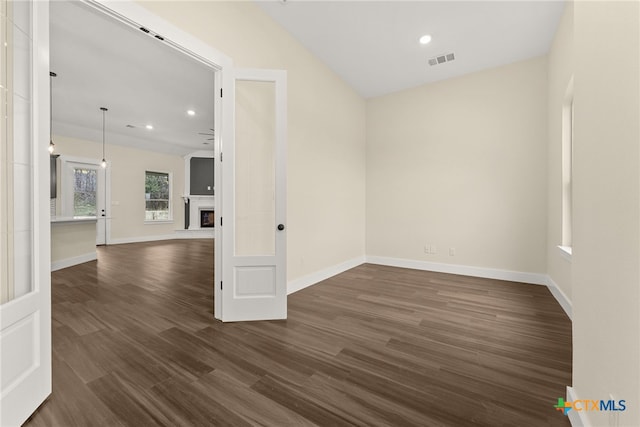 empty room with dark wood-style floors, visible vents, a fireplace with raised hearth, and baseboards