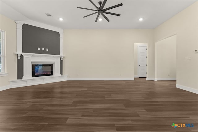 unfurnished living room featuring dark wood-type flooring, a glass covered fireplace, visible vents, and a ceiling fan