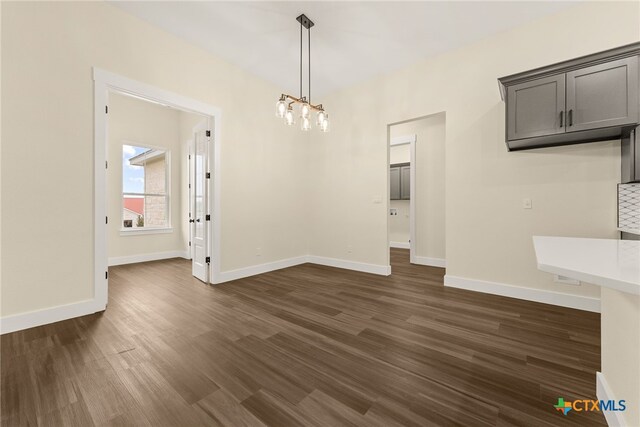 unfurnished dining area featuring a notable chandelier, dark wood-type flooring, and baseboards