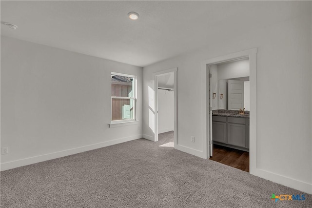 unfurnished bedroom featuring connected bathroom, a walk in closet, a closet, and dark colored carpet