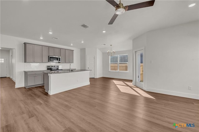 kitchen featuring stainless steel appliances, gray cabinets, an island with sink, and a wealth of natural light