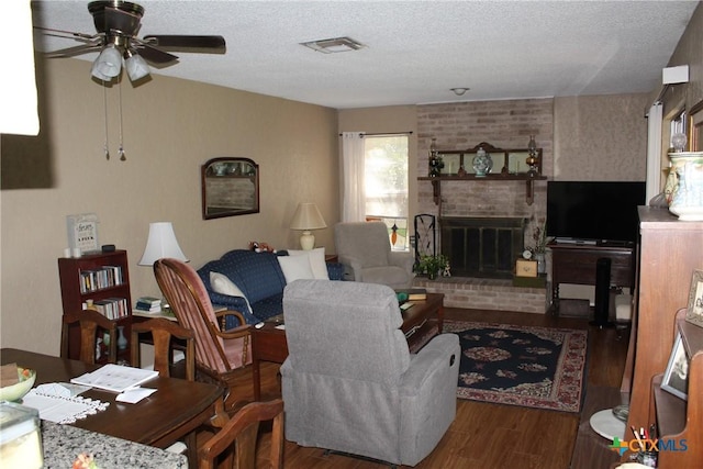 living area with ceiling fan, a brick fireplace, wood finished floors, and a textured ceiling