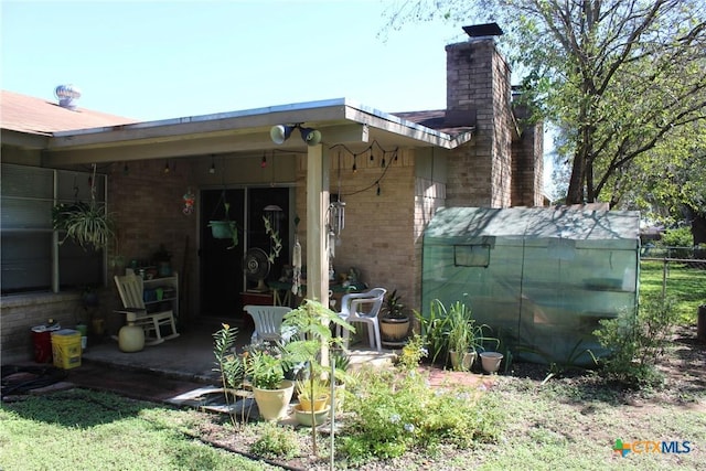 rear view of house featuring brick siding, a chimney, and fence