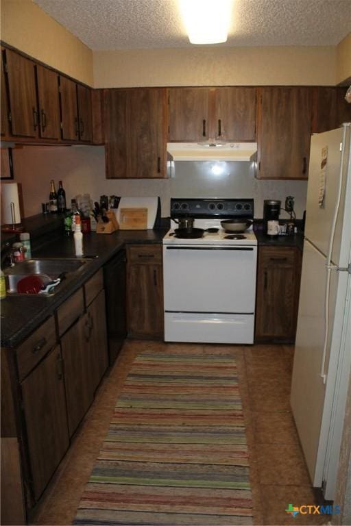 kitchen featuring under cabinet range hood, white appliances, dark countertops, and a sink