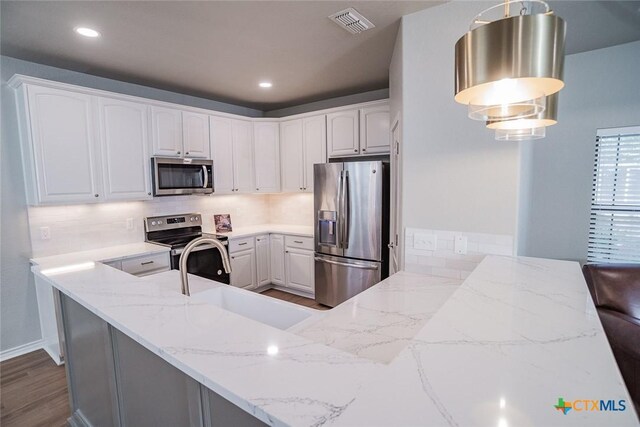 kitchen featuring appliances with stainless steel finishes, white cabinetry, a peninsula, and a sink