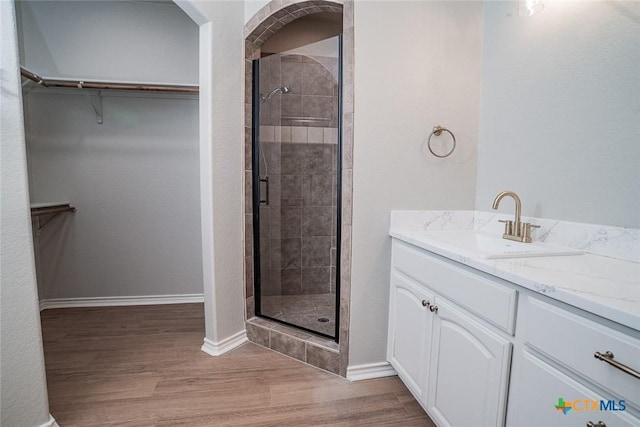 bathroom featuring a walk in closet, wood finished floors, a stall shower, and baseboards