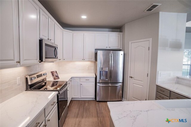 kitchen with tasteful backsplash, white cabinetry, stainless steel appliances, light wood-style floors, and light countertops